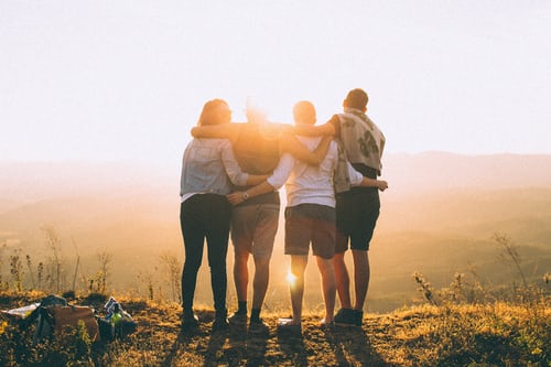 Four people facing the sunset with arms behind each others backs