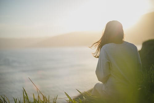 Woman on cliff side looking out into sunset